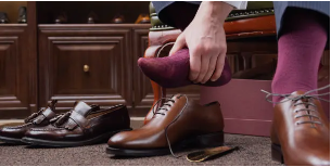 Man getting ready, wearing shoes beside a pair of brown shoes,