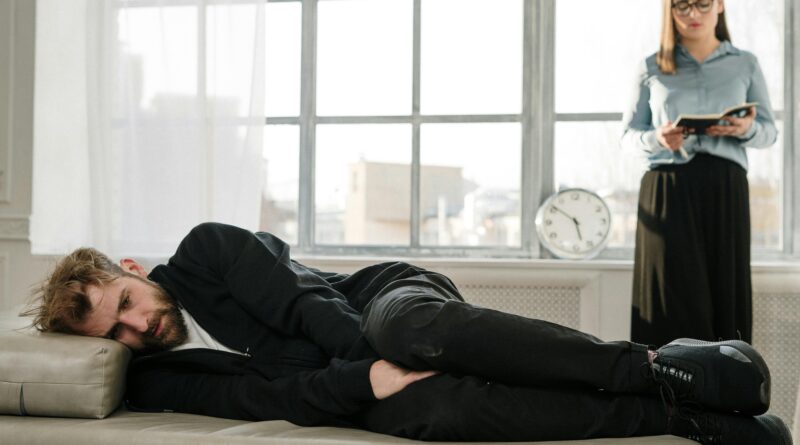 A woman stands behind a man sleeping on a couch.